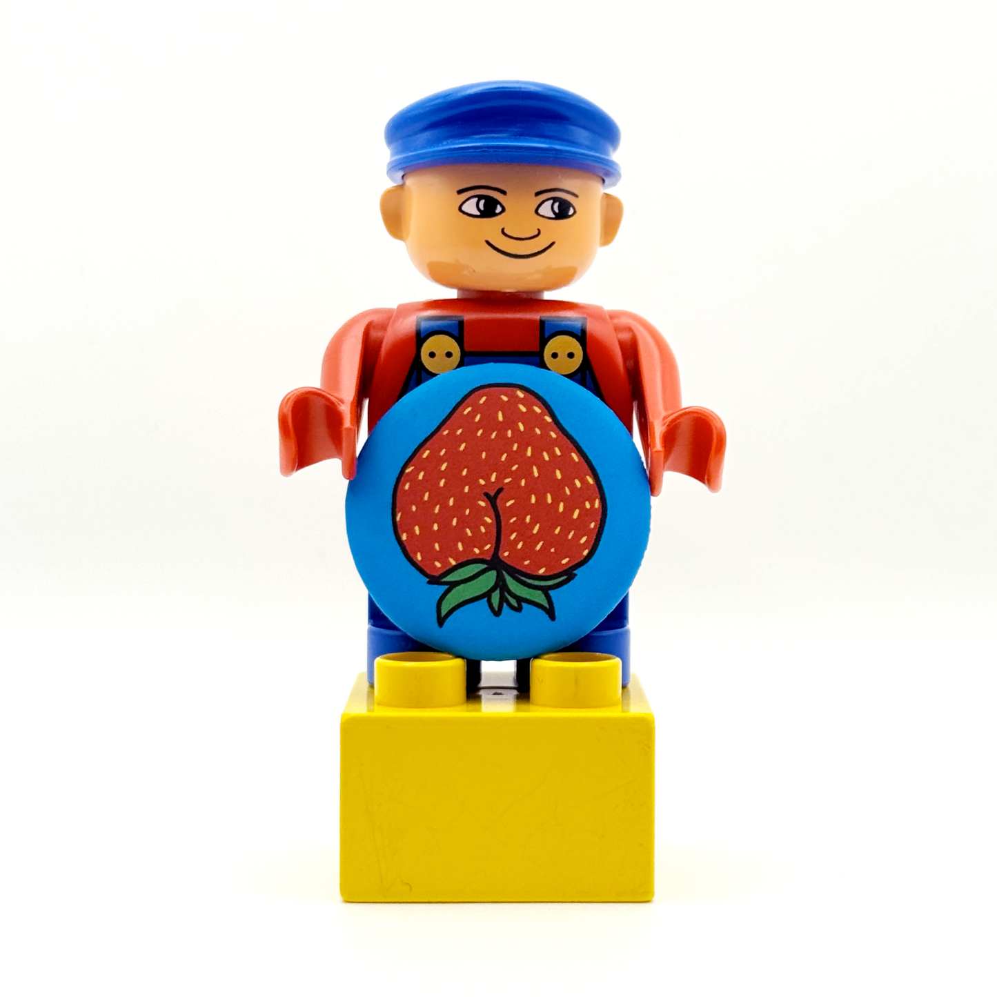 It's a Duplo worker toy holding a fruity and fancy tiny ass magnet. The magnet features a strawberry with an asscrack with a matte finish. 
