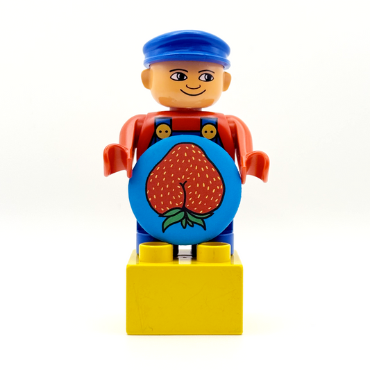 It's a Duplo worker toy holding a fruity and fancy tiny ass magnet. The magnet features a strawberry with an asscrack with a matte finish. 